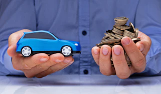 Hands holding toy car and pile of coins